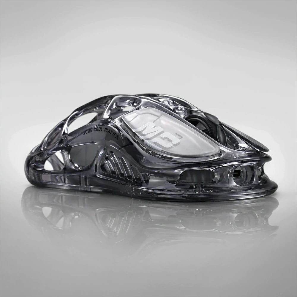 GravaStar Mercury M2 Transparent Black gaming mouse, a 2024 Red Dot Award-winning design featuring a sleek transparent black finish with ambidextrous ergonomic shape, compatible with palm, tip, and claw grips. Equipped with the high-precision PAW3395 sensor (26,000 DPI, 650 IPS acceleration, 1,000 Hz wireless polling rate) for pixel-perfect tracking, plus 82 hours of battery life (USB-C wired/Bluetooth 5.1). Highlighted specs: 5 programmable buttons with macro support, 5 customizable RGB lighting modes (16.